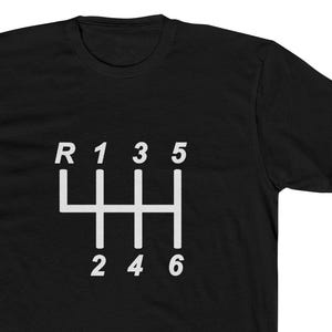 May include: Black t-shirt with a white graphic of a car's manual transmission gear shift pattern. The shift pattern includes the reverse gear, first through sixth gears, and is centered on the shirt.