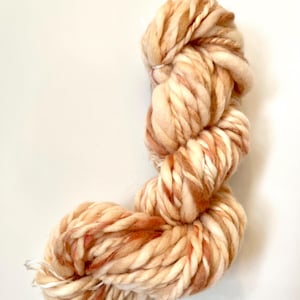Puede incluir: Un gran ovillo de lana gruesa en tonos crema, beige y óxido. La lana gruesa y texturizada está bien enrollada y parece suave. Las variaciones de color crean un efecto veteado, ideal para proyectos de punto o ganchillo.