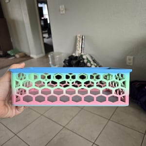 May include: A rectangular storage basket featuring a honeycomb lattice pattern. The basket displays a gradient color scheme that transitions from a light blue top rim to a green middle section and a pink base, constructed with a rigid open-frame design.