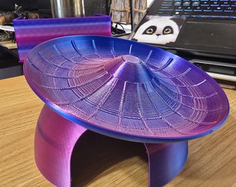 May include: A 3D printed object featuring a wide, circular, concave top disc with a radial web-like pattern, supported by a dome-shaped base with an arched opening. The piece displays a gradient color transition from deep blue to magenta.