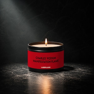 May include: A black metal candle tin with a red label featuring the black text "CHARLES' PODIUM MANIFESTATION FLAME" and "LAZEFLAME". The candle has a single lit wick with a visible flame, and the wax inside the container is white.
