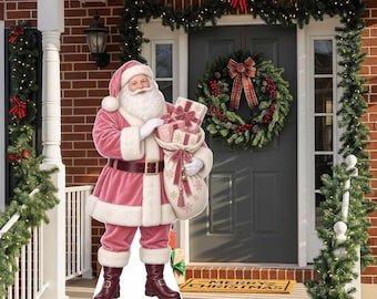 May include: A life-sized cardboard cutout of Santa Claus wearing a pink suit with white fur trim, holding a sack of gifts. The figure stands on a porch with a brick wall, a dark grey door, a green wreath, and green garland decorations.
