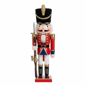 May include: A decorative wooden nutcracker soldier in a classic design. The figure is dressed in a red jacket with gold accents, a black hat, and white pants. It holds a rifle and stands on a red base. A festive holiday decoration.