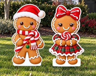 May include: Two gingerbread person lawn decorations. One wears a red Santa hat and a red and white striped scarf while holding a candy cane. The other wears a large red bow and a red and green plaid dress while holding a red and white lollipop.