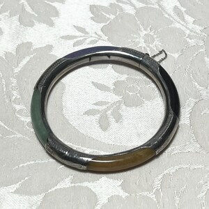May include: A hinged bangle bracelet featuring alternating segments of polished silver-tone metal and smooth, rounded stone inserts in shades of green, black, brown, and purple. The bracelet includes a secure clasp mechanism and a small safety chain.