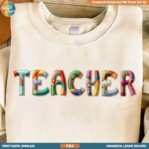 May include: Cream-colored sweatshirt with the word "TEACHER" embroidered in colorful, psychedelic-style letters. The letters feature a variety of patterns and colors, including teal, orange, green, and purple. The sweatshirt has a crew neck.