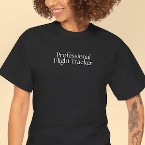 Puede incluir: Camiseta negra con el texto blanco "Professional Flight Tracker". La camiseta es de cuello redondo y la lleva una persona con vaqueros azules.