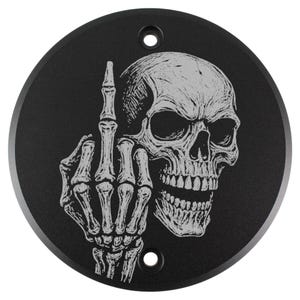 Peut inclure: Plaque métallique noire et circulaire avec une illustration détaillée en gris clair d'un crâne humain et d'une main squelettique faisant un geste obscène. La plaque comporte deux petits trous pour le montage.