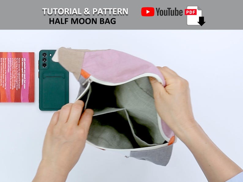 May include: A half moon bag with a zipper closure and multiple compartments. The bag is made of a light gray fabric with a pink and beige fabric flap. The bag is open and a hand is reaching inside.