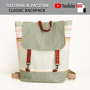 May include: A green, white, and pink striped fabric backpack with brown leather straps and buckles. The backpack has a flap closure and a large pocket on the front.