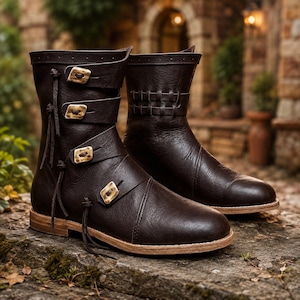 May include: A pair of dark brown mid-calf boots featuring four horizontal straps secured with light-coloured rectangular buckles. The boots have a smooth finish, rounded toes, and a light tan sole, with leather laces tied along the side.
