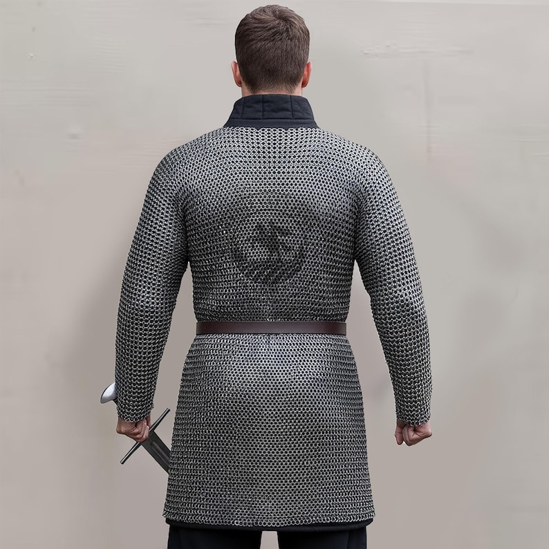 May include: A silver chainmail shirt with long sleeves and a brown belt. The shirt has a black collar and a design on the back. A sword is held in the right hand. The image is of a medieval garment.