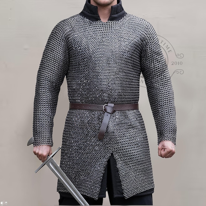 May include: A silver chainmail shirt with long sleeves and a black collar. A brown leather belt is worn around the waist. The person is holding a silver sword. The shirt is a historical garment.