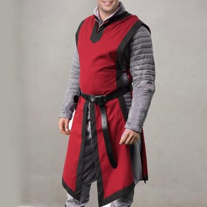 May include: A red and black medieval tunic with a black belt. The tunic has a V-neck and is layered over a gray quilted undershirt. The outfit is designed for historical reenactment or costume use.