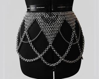 May include: A silver chainmail belt with a geometric design. The belt is made of small, interlocking metal rings and hangs from a black belt that reads "WAIST". The chainmail forms a skirt-like shape.
