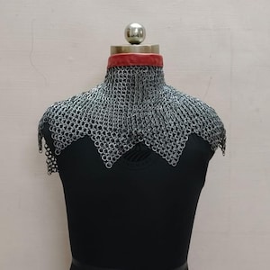 Könnte beinhalten: Ein Kettenhaubenkragen, eine Art mittelalterlicher Rüstung, wird auf einer schwarzen Schaufensterpuppe ausgestellt. Die Haube besteht aus kleinen, ineinandergreifenden Metallringen mit einem roten Lederkragen. Die Kettenrüstung bedeckt Hals und Schultern.