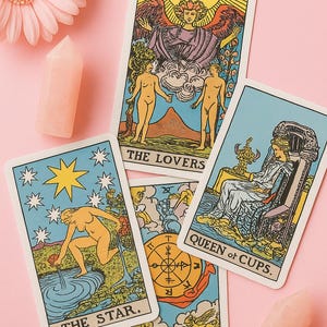 May include: Tarot cards featuring illustrations and text such as "The Lovers," "The Star," "Queen of Cups," and "Queen of Fortune." The cards are displayed on a pink surface, accompanied by a pink flower and two crystal points.