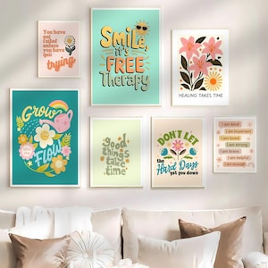 May include: A collection of framed art prints with inspirational quotes and floral designs. The prints feature phrases like "Smile, it's free therapy" and "Grow with the flow." Colors include teal, pink, yellow, and white. The prints are displayed on a white wall.