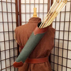 May include: A green leather quiver with a brown leather flap, holding a bundle of wooden arrows with white fletching. The quiver is worn on a brown garment with a brown leather belt.