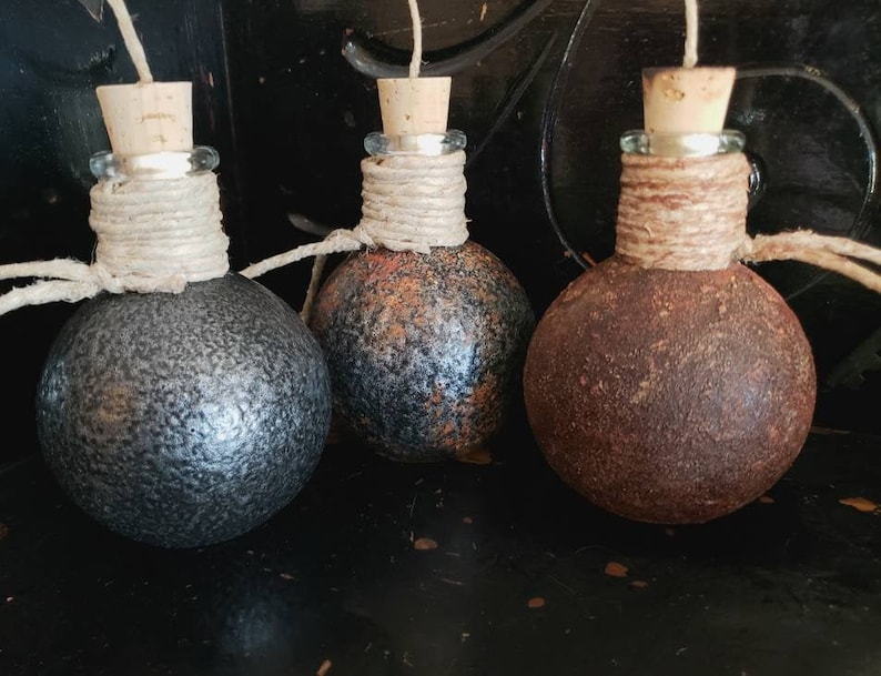 May include: Three round glass bottles with cork stoppers and twine wrapped around the necks. The bottles are painted in different shades of brown, black, and gray, giving them a rustic and aged look.