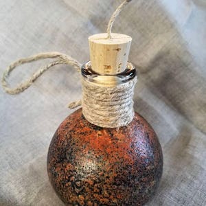 May include: A small, round, orange and black bottle with a cork stopper and a piece of twine tied around the neck.
