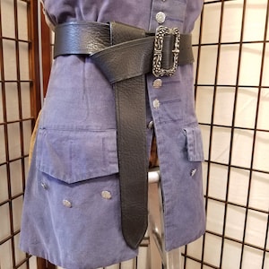 以下が含まれることがあります： 花柄の銀色のバックルが付いた黒い革のベルト。ベルトは青いシャツに巻き付けられ、結び目で固定されています。