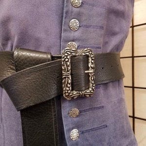 以下が含まれることがあります： 銀色の装飾的なバックルが付いた黒い革のベルト。バックルは正方形で、複雑な花の模様が施されています。