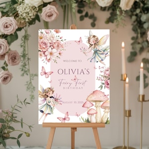 May include: A wooden easel displays a pink and white sign for Olivia's Fairy First Birthday. The sign features illustrations of fairies, butterflies, flowers, and mushrooms. The text reads "Welcome to Olivia's Fairy First Birthday, August 10, 2025."