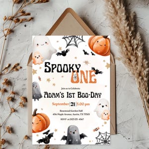 May include: A Halloween-themed invitation card featuring the text "SPOOKY ONE" and "Adam's 1st Boo-Day." The design incorporates illustrations of ghosts, pumpkins, bats, and spiderwebs. The invitation is set against a neutral background with decorative elements.