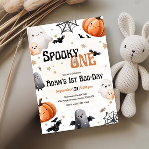 May include: A Halloween party invitation with the words "Spooky One" and "Adam's 1st Boo-Day". The design features illustrations of ghosts, bats, pumpkins, and spiderwebs. The invitation is on a white background with gold stars.
