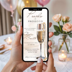 K&ouml;nnte beinhalten: Ein Smartphone zeigt eine digitale Einladung f&uuml;r eine Hochzeitsfeier. Die Einladung zeigt den Text "Pearls & Prosecco" &uuml;ber einem Sektglas mit einer Perlenkette. Die Einladung enth&auml;lt den Namen der Braut, Datum, Uhrzeit und Veranstaltungsort.