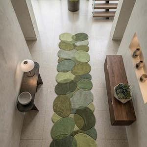 May include: A long, rectangular runner rug featuring an organic pattern of overlapping circular and pebble-shaped sections in various shades of green, ranging from light lime to deep forest tones. The text RugsByRubina is visible at the bottom.