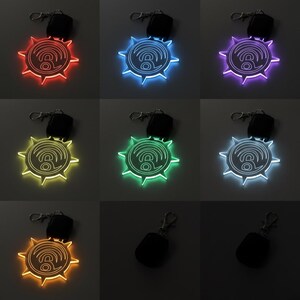 May include: A collection of illuminated keychains in various colors, including red, blue, purple, green, yellow, and white. Each keychain features a sunburst design with a central symbol and a remote control.