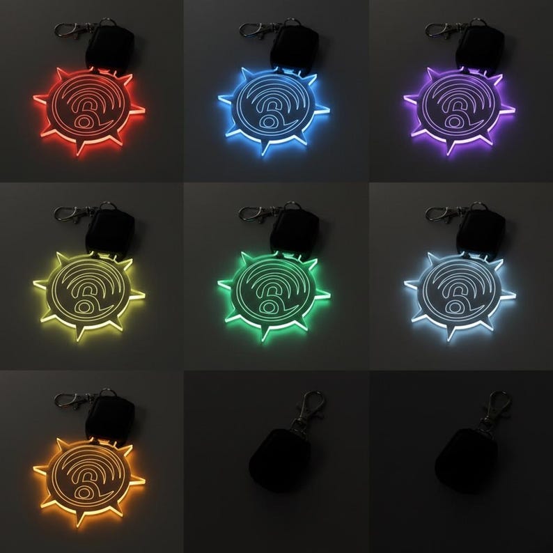 May include: A collection of illuminated keychains in various colors, including red, blue, purple, green, yellow, and white. Each keychain features a sunburst design with a central symbol and a remote control.