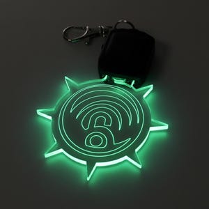 May include: A glowing green keychain with a stylized wifi symbol and a lock icon. The keychain is shaped like a sunburst and is attached to a silver keyring and a black remote.