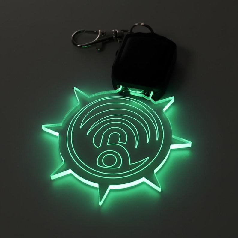 May include: A glowing green keychain with a stylized wifi symbol and a lock icon. The keychain is shaped like a sunburst and is attached to a silver keyring and a black remote.