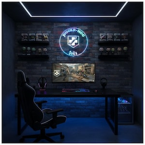 Könnte beinhalten: Ein Gaming-Setup mit einem schwarzen Schreibtisch, Stuhl und Monitor. Die Backsteinmauer hat ein Neon-Schild "JUGGER-NOG Soda" und Regale mit Figuren. Der Raum wird von blauen und weißen Neonlichtern beleuchtet.