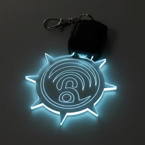 May include: A glowing, clear acrylic keychain with a stylized wifi symbol design. The keychain has a starburst shape with pointed edges and a silver clasp. A black remote is attached to the keychain.