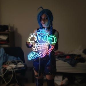 Może przedstawiać: Neonowy znak w kształcie postaci z kreskówki ze słowem "BOOM" w kolorowym gradiencie. Znak jest trzymany przed osobą. Znak ma czarny kontur i jest podświetlony tęczą kolorów.