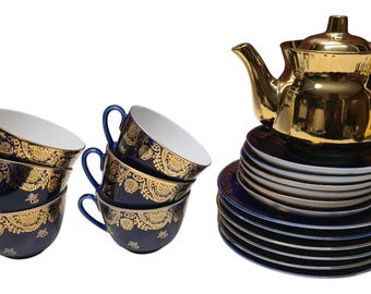 May include: A tea set featuring navy blue cups and saucers with gold floral designs. A gold teapot sits atop a stack of plates. The set includes six cups and a variety of plates.