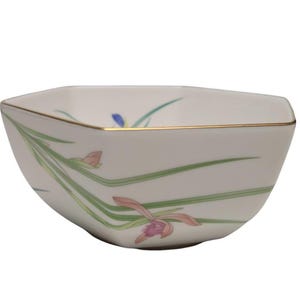 May include: A square, cream-coloured ceramic bowl with a gold rim. The bowl is decorated with a floral design featuring pink and purple orchids, green leaves, and blue accents. The bowl has a modern, geometric shape.