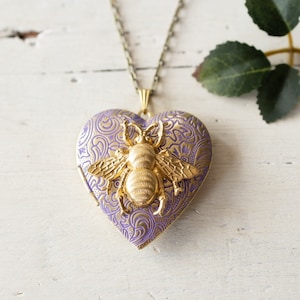 May include: A gold heart-shaped locket necklace with a purple filigree design and a gold bee charm.