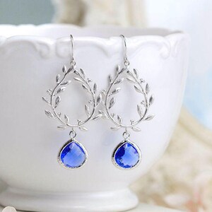 May include: Silver earrings with a delicate leaf design and a dangling blue teardrop-shaped crystal.