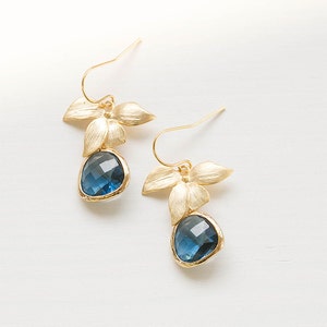Puede incluir: Pendientes de oro con gotas de piedras preciosas azules y detalles de flores doradas.