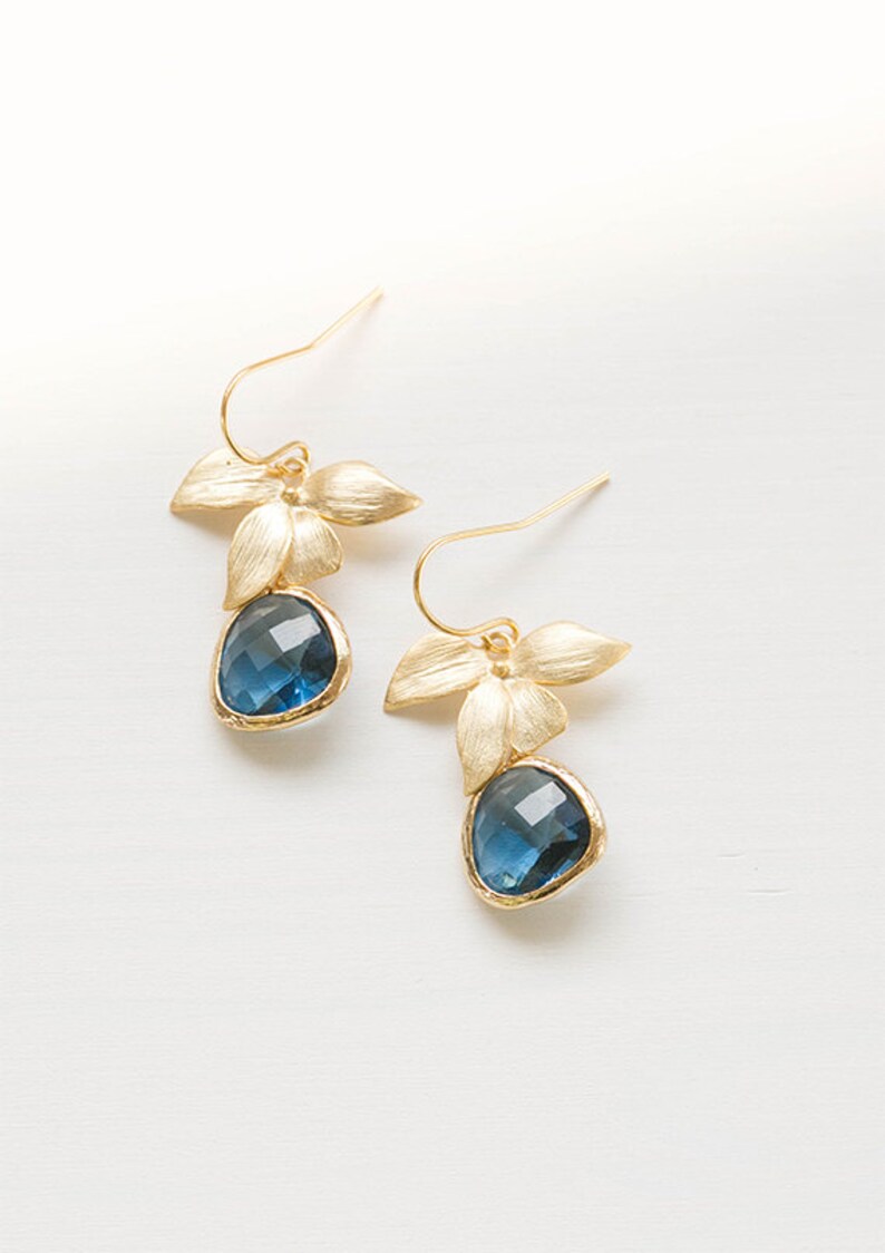 Puede incluir: Pendientes de oro con gotas de piedras preciosas azules y detalles de flores doradas.