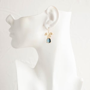 Puede incluir: Pendientes de oro con una piedra preciosa azul y detalles de hojas.