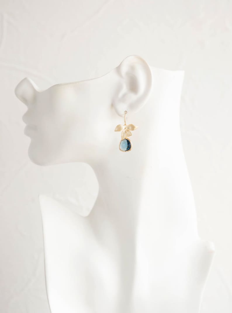 Puede incluir: Pendientes de oro con una piedra preciosa azul y detalles de hojas.