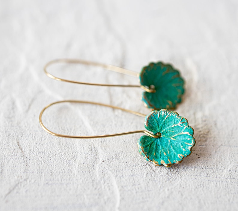 Op de afbeelding: Een paar gouden oorbellen met turquoise groene bladeren. De oorbellen zijn gemaakt van draad en hebben een eenvoudig ontwerp.
