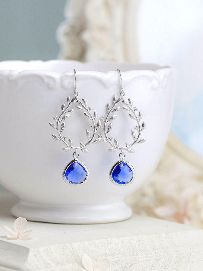 May include: Silver earrings with a delicate leaf design and a dangling blue teardrop-shaped crystal.