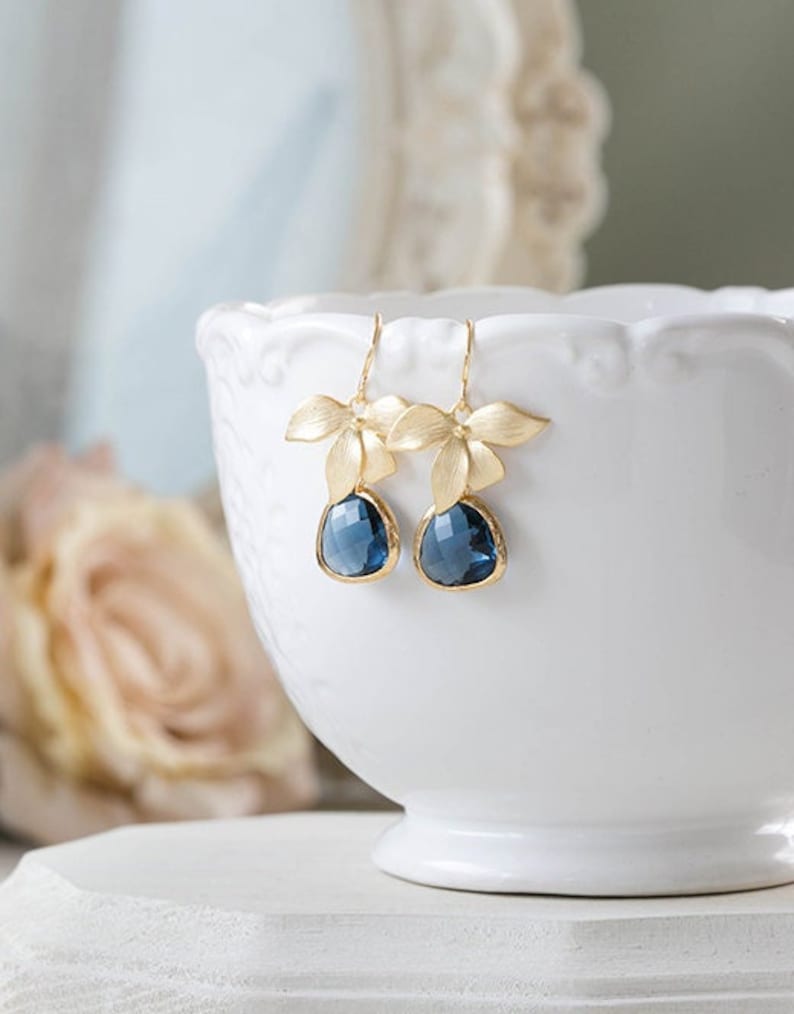 Puede incluir: Pendientes de oro con cristales azules en forma de l&aacute;grima y delicados detalles florales.